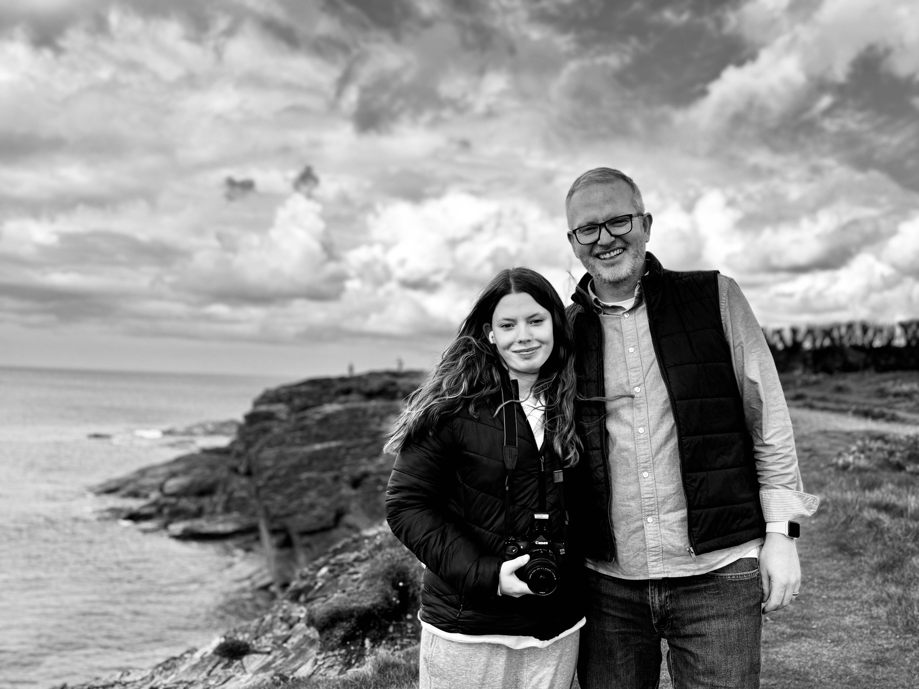 Sam and Eloise standing together on a rocky coastline with a cloudy sky in the background.